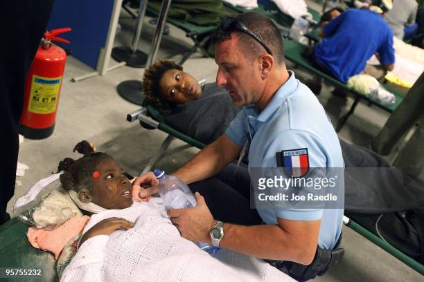 An injured girl is given water by a French aid worker at a makeshift field hospital on January 13, 2010 in Port-au-Prince, Haiti. Planeloads of...