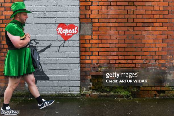 Man wearing a leprechaun dress walks in front of a pro-choice mural based on a work by Banksy urging a yes vote in the referendum to repeal the...