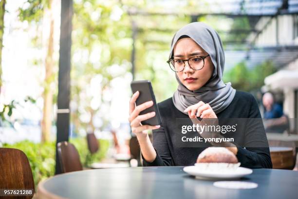 muslim girl feeling confused with her smartphone - asian waiting angry expressions stock pictures, royalty-free photos & images