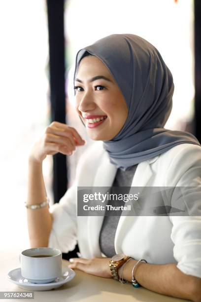 young muslim woman enjoying coffee in a cafe - malaysian culture stock pictures, royalty-free photos & images