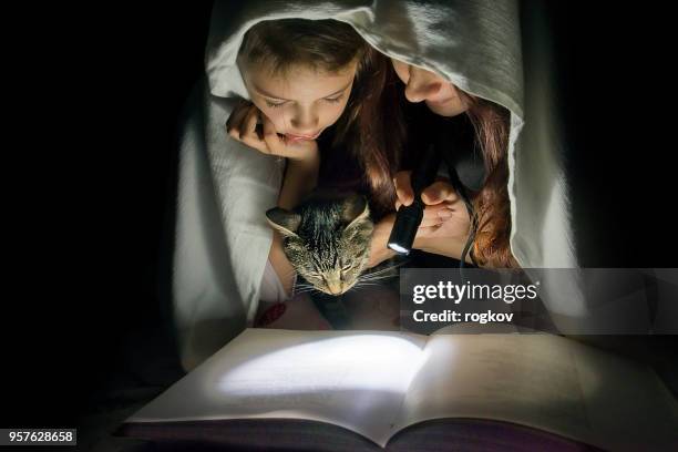 mom and daughter read fairy tales in the dark under a blanket covering the book with a flashlight. - kids fort stock pictures, royalty-free photos & images