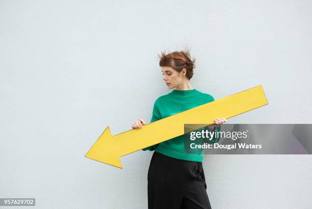 young woman holding large yellow arrow sign pointing down. - verringerung stock-fotos und bilder