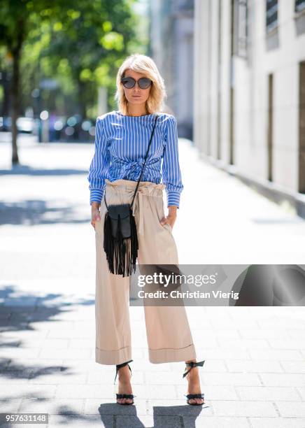 Gitta Banko wearing a blue and white striped blouse with front-knot detail and beige-colored, flared trousers by GR8FUL, black mini fringed leather...