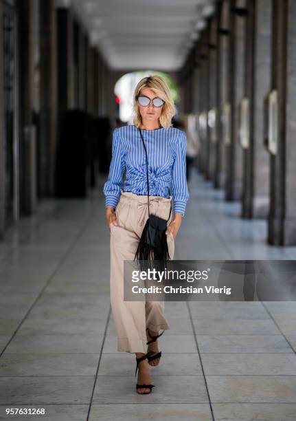 Gitta Banko wearing a blue and white striped blouse with front-knot detail and beige-colored, flared trousers by GR8FUL, black mini fringed leather...