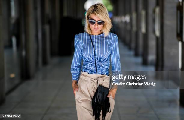 Gitta Banko wearing a blue and white striped blouse with front-knot detail and beige-colored, flared trousers by GR8FUL, black mini fringed leather...