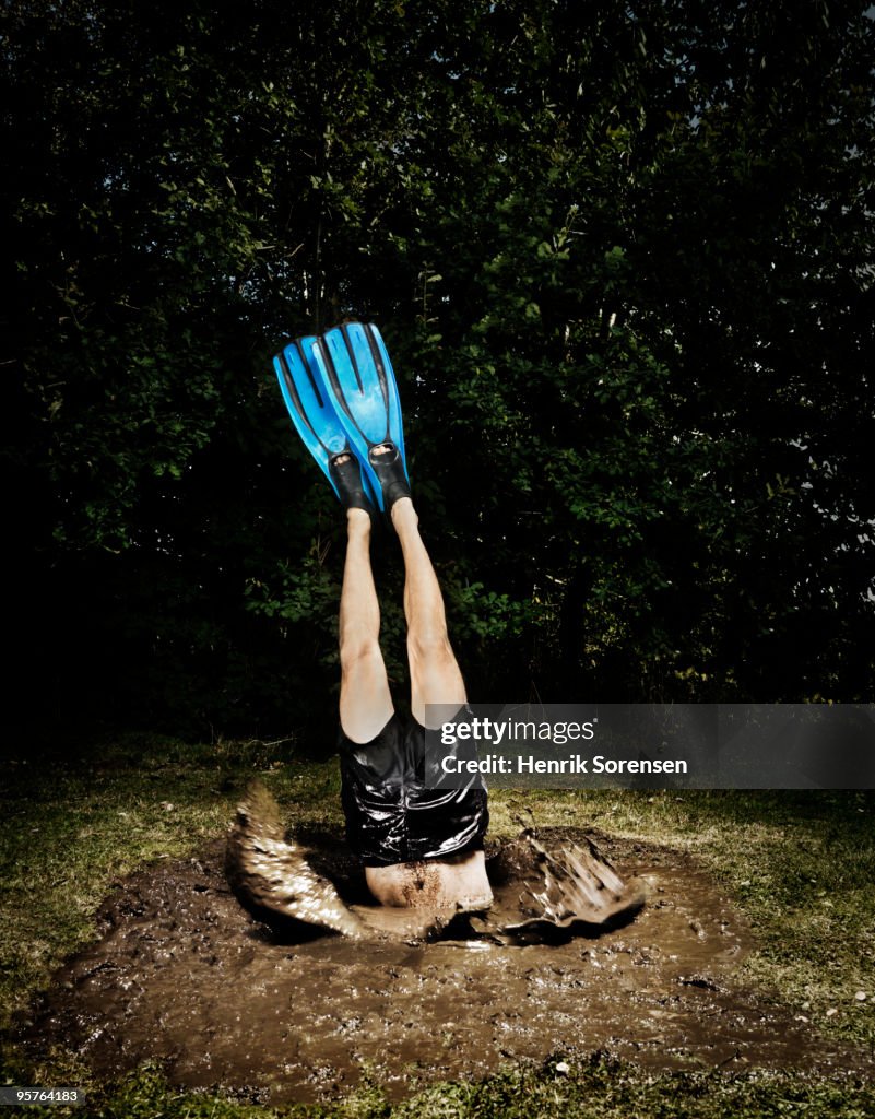 Male diver with flippers dives into mud hole