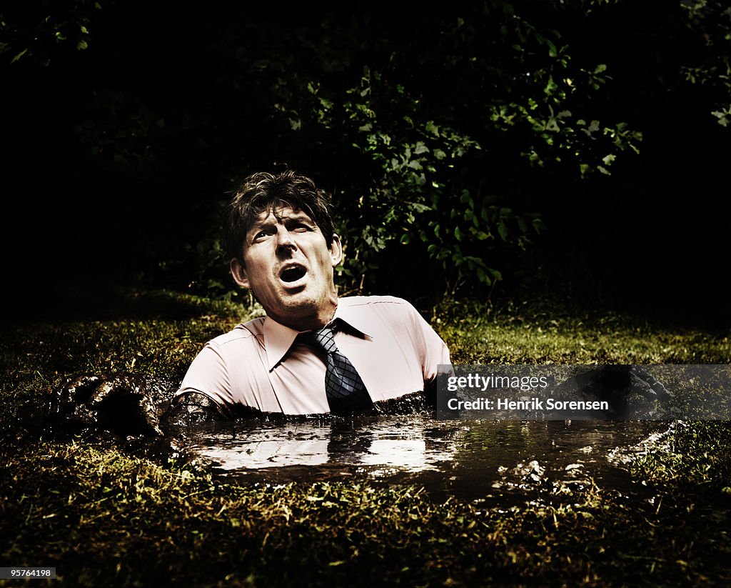 Businessman sinking in a mud hole