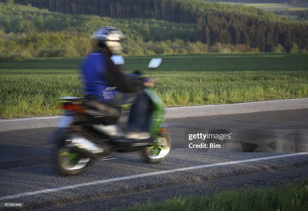 Teen riding Hause auf seinem moped, motion blur