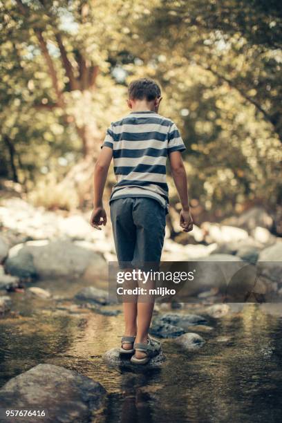 little boy crossing over creek - miljko stock pictures, royalty-free photos & images