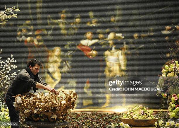 An artist works on a floral arrangement in front of a reproduction, made up of thousands of tiny painted wooden clogs, of Rembrandt's painting "The...