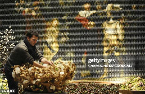 An artist works on a floral arrangement in front of a reproduction, made up of thousands of tiny painted wooden clogs, of Rembrandt's painting "The...