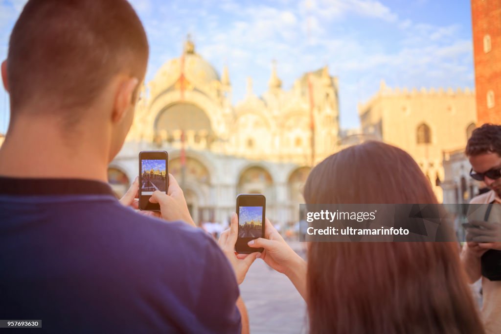 Touristen in Venezia. Junge Frauen und junge Männer, viel Spaß. Paar ein Foto mit Smartphone, St.-Markus Kathedrale auf der Piazza San Marco, Venedig. Lässigen Lebensstil Städtisches Motiv Italien.  Besuch in Venedig, Italien.