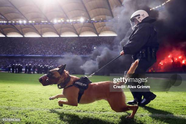 Police dog is seen on the pitch as fans throw flares during the Bundesliga match between Hamburger SV and Borussia Moenchengladbach at...