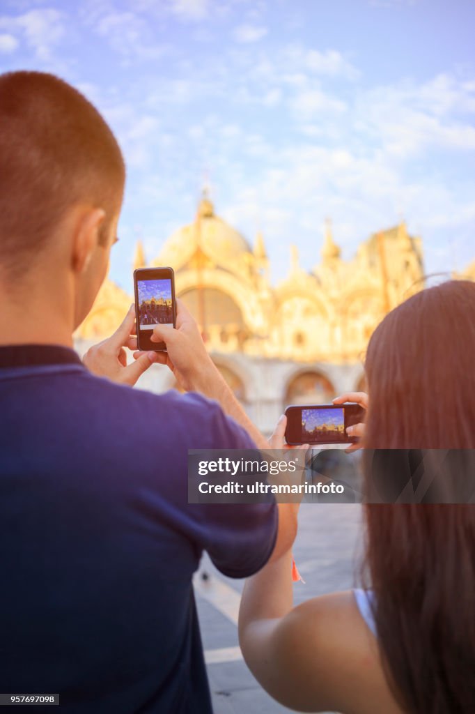 Touristen in Venezia. Junge Frauen und junge Männer, viel Spaß. Paar ein Foto mit Smartphone, St.-Markus Kathedrale auf der Piazza San Marco, Venedig. Lässigen Lebensstil Städtisches Motiv Italien.  Besuch in Venedig, Italien.