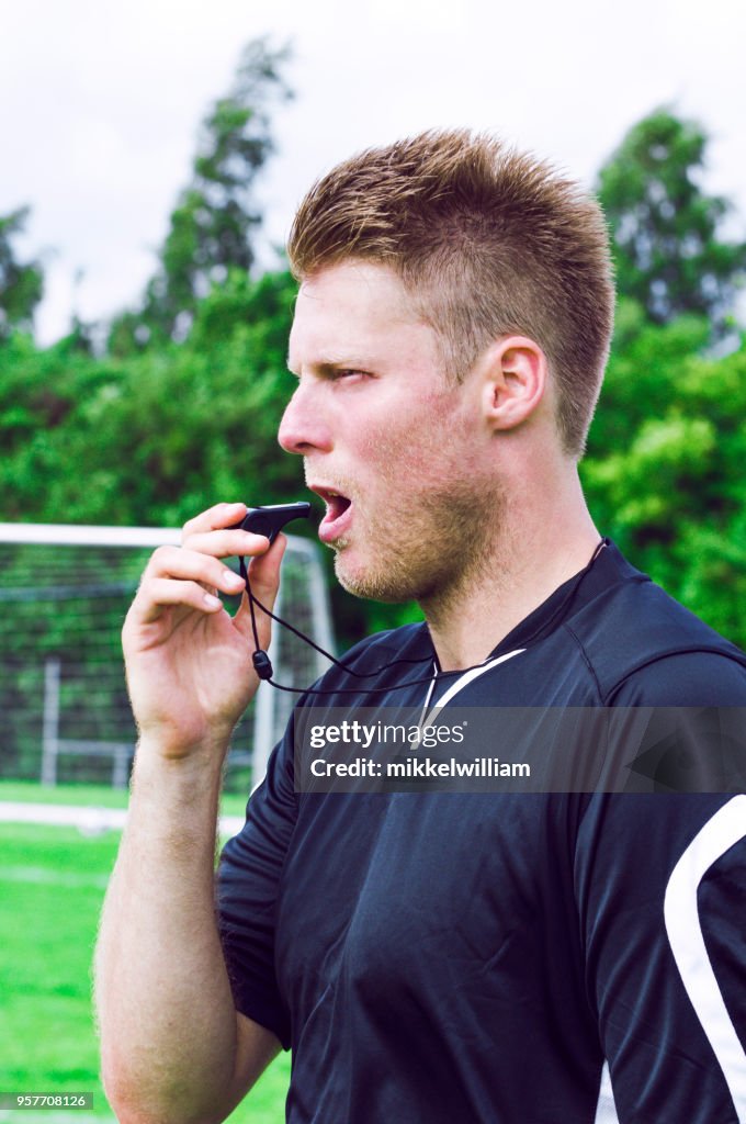 Sports referee sees a fault during a match and blows whistle