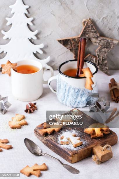 Shortbread Christmas cookies for cups, two cups of hot tea and sugar powder over table with white tablecloth with Christmas decor at background....