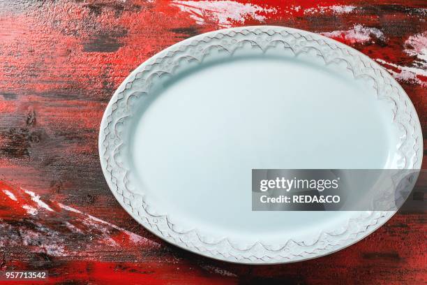 Empty blue ceramic oval plate with ornament over red-black wooden background. Top view.