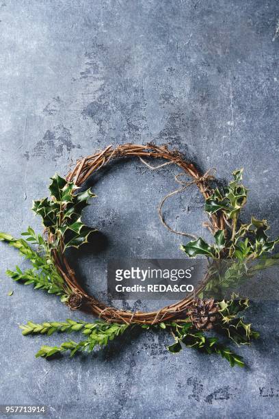 Simple handmade Christmas wreath with green branches and cones over blue texture background. Top view, copy space. Christmas greeting card.