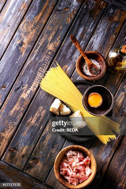 Ingredients for traditional italian pasta alla carbonara. Uncooked spaghetti, pancetta bacon, parmesan cheese, egg yolk, salt, pepper in olive wood...