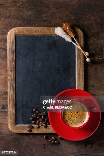 Empty vintage chalkboard, coffee beans, crystal sugar, and red cup of black coffee over old wooden background. Top view with space for text.