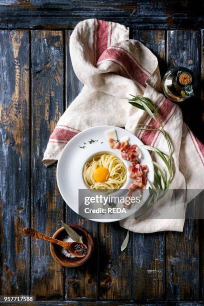 Italian traditional pasta alla carbonara with yolk, pancetta bacon, parmesan cheese, thyme, served in white plate on textile over old wooden plank...
