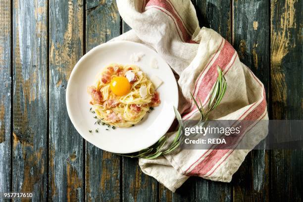 Italian traditional pasta alla carbonara with yolk, pancetta bacon, parmesan cheese, thyme, served in white plate on textile linen over old wooden...