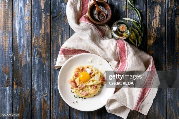 Italian traditional pasta alla carbonara with yolk, pancetta bacon, parmesan cheese, thyme, served in white plate on textile over old wooden plank...