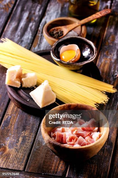 Ingredients for traditional italian pasta alla carbonara. Uncooked spaghetti, pancetta bacon, parmesan cheese, egg yolk, salt, pepper in olive wood...