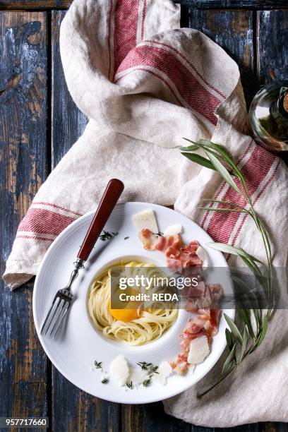 Italian traditional pasta alla carbonara with yolk, pancetta bacon, parmesan cheese, thyme, served in white plate on textile linen over old wooden...