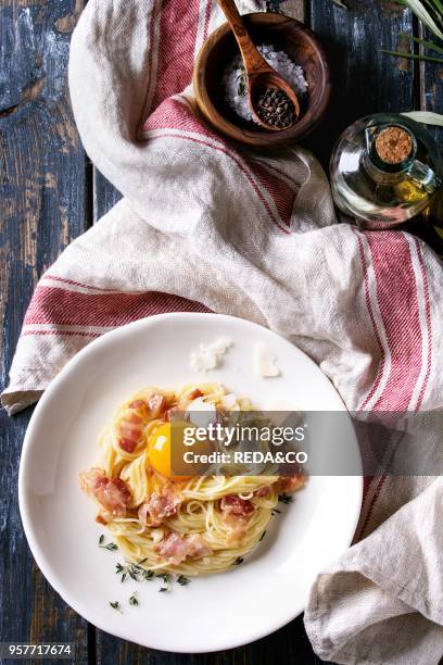 Italian traditional pasta alla carbonara with yolk, pancetta bacon, parmesan cheese, thyme, served in white plate on textile over old wooden plank...