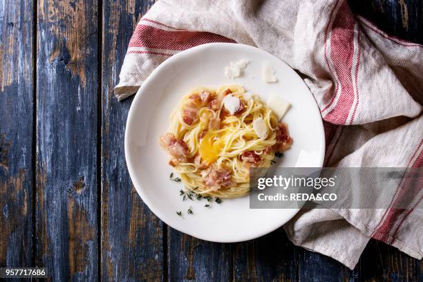 Italian traditional pasta alla carbonara with yolk, pancetta bacon, parmesan cheese, thyme, served in white plate on textile linen over old wooden...