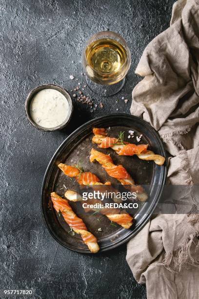 Appetizer with smoked salmon on crispy breadsticks served on vintage metal tray with cheese dill sauce, sea salt, glass of white wine, textile napkin...