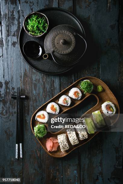 Homemade sushi rolls set with salmon, sesame seeds and avocado serving in wood plate with pink pickled ginger, soy sauce, wasabi, seaweed salad,...