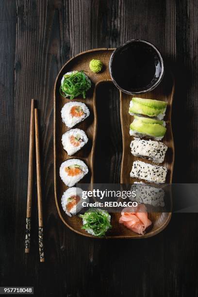 Homemade sushi rolls set with salmon, sesame seeds and avocado serving in wood plate with pink pickled ginger, soy sauce, wasabi, seaweed salad,...