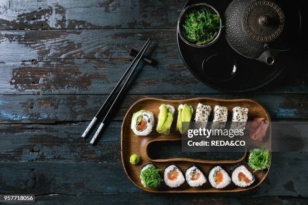 Homemade sushi rolls set with salmon, sesame seeds and avocado serving in wood plate with pink pickled ginger, soy sauce, wasabi, seaweed salad,...