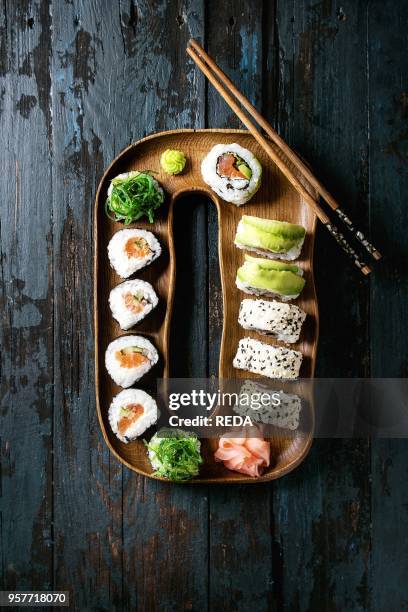 Homemade sushi rolls set with salmon, sesame seeds and avocado serving in wood plate with pink pickled ginger, soy sauce, wasabi, seaweed salad,...