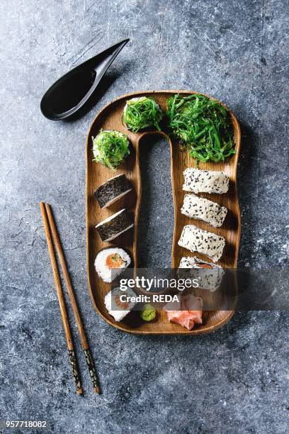 Homemade sushi rolls set with salmon, sesame seeds serving in wooden plate with pink pickled ginger, soy sauce, wasabi, seaweed salad, chopsticks on...