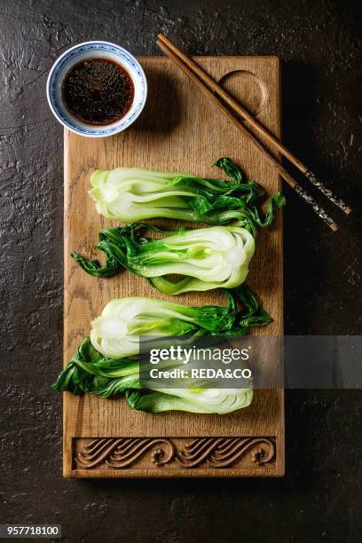 Stir fried bok choy or chinese cabbage with soy sauce served on decorative wooden cutting board with chopsticks over dark texture background. Top...