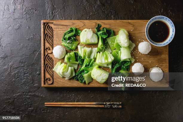 Stir fried bok choy or chinese cabbage with soy sauce and rice balls served on decorative wooden cutting board with chopsticks over dark texture...