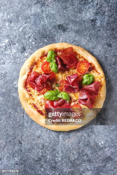 Traditional pizza with bresaola, cheese, tomatoes and basil over blue texture background. Top view with space.