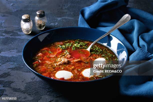 Plate of traditional beetroot borscht soup with sour cream and fresh coriander served with garlic bread buns pampushka with blue textile over dark...