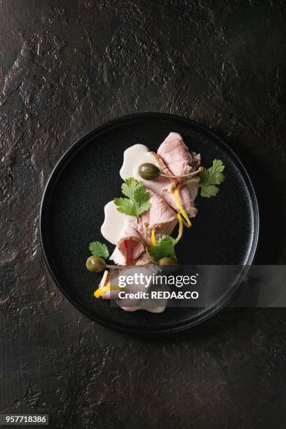 Vitello tonnato italian dish. Thin sliced veal with tuna sauce, capers and coriander served on black plate over dark texture background. Top view,...