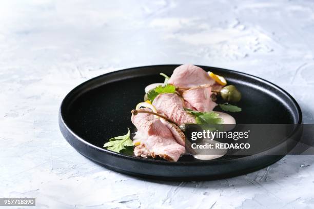 Vitello tonnato italian dish. Thin sliced veal with tuna sauce, capers and coriander served on black plate over gray texture background.