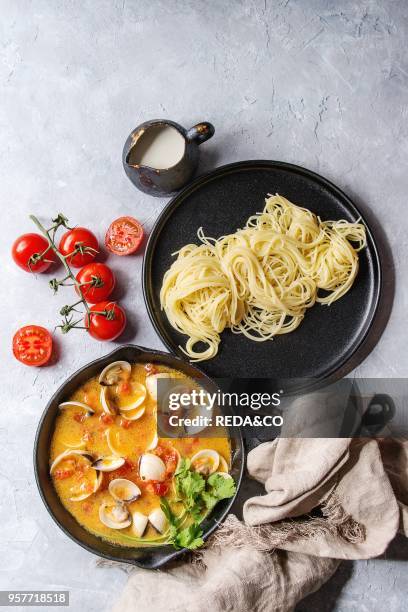 Vongole in tomato cream sauce for pasta in cast-iron pan with textile and black plate with cooked spaghetti over gray texture background. Top view,...