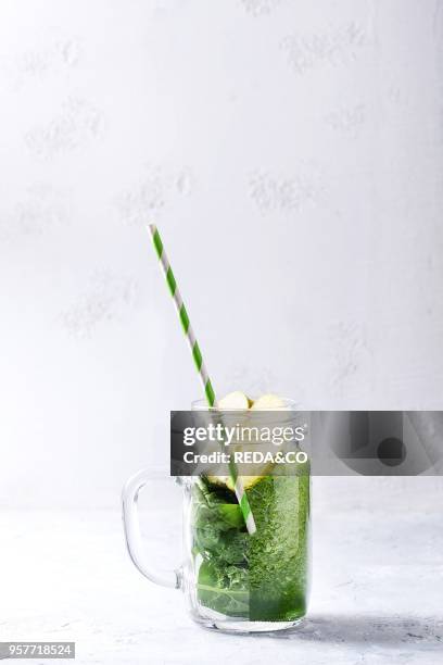 Detox drink concept. Ingredients green spinach leaves and apple and shaked smoothie in one mason jar with retro cocktail tube over white texture...