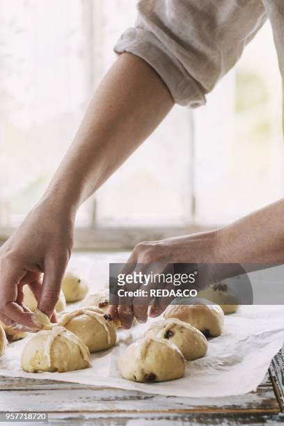 Raw unbaked buns. Ready to bake homemade Easter traditional hot cross buns on baking paper over white wooden table. Window at background. Female...