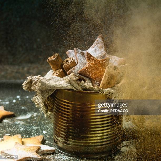 Homemade shortbread star shape sugar cookies with sugar and cinnamon sprinkling powder in old tin can sackcloth rag with cinnamon sticks on dark...