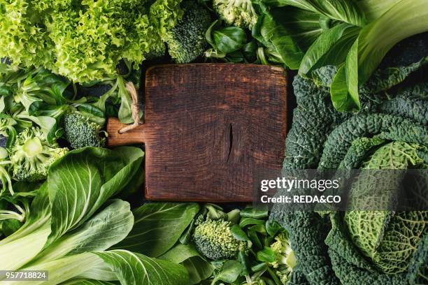 Variety of raw green vegetables salads. Lettuce. Bok choy. Corn. Broccoli. Savoy cabbage round empty wooden chopping board. Food background. Top...