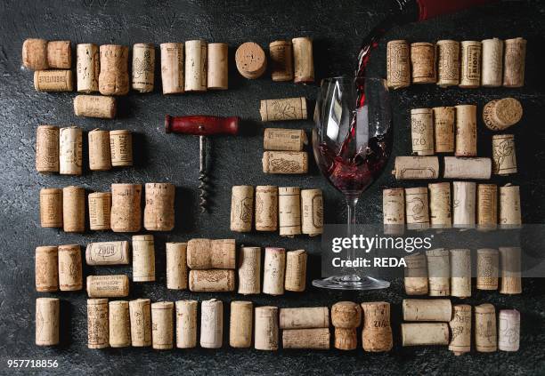 Big set of used wine corks in rows with vintage corkscrew and pouring red wine in glass over black texture background. Top view.