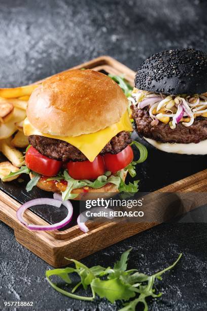 Homemade traditional hamburger with beef, tomato, cheese, aragula, served on wooden slate serving board with french fries and ketchup sauce on dark...